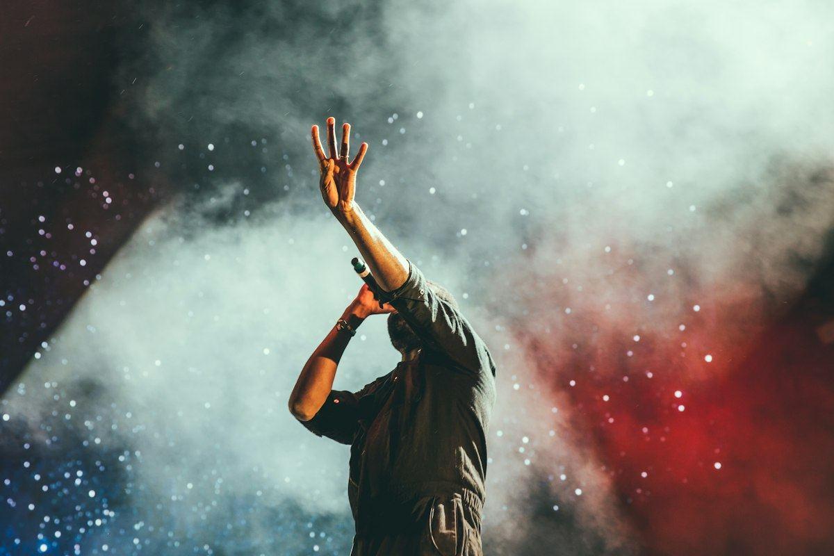 A performer with one hand raised on a smoky stage